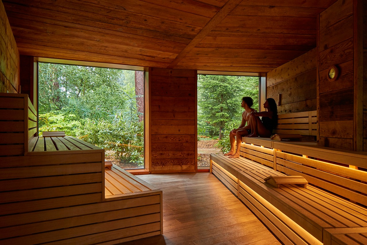 Couple sitting in the Nordic Sauna enjoying views of the forest.